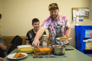 A man serves plates of food to a table of young people