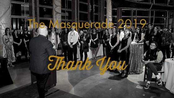 black and white image of a man speaking in front of a large crowd dressed in costumes and gala attire. Gold text reads The Masquerade 2019 thank you.