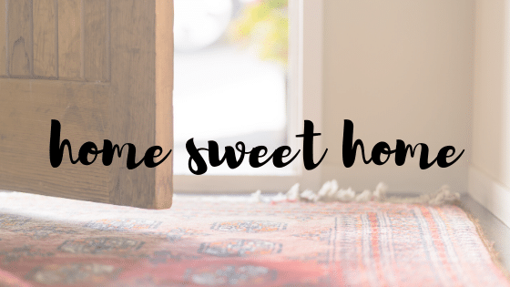 a brown wooden door is partially open to the outside. a red patterned rug sits on the floor. we have written the words "home sweet home" in black text over the image