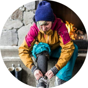 A photograph of Youth Worker, Bridgit Muldoon. She is wearing brightly coloured ski clothes and lacing up her snowboard boots