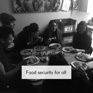 A group of young people sit around a dining table loaded with yummy food. They look happy.