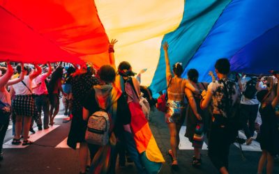 A group of people walk beneath a giant rainbow flag.