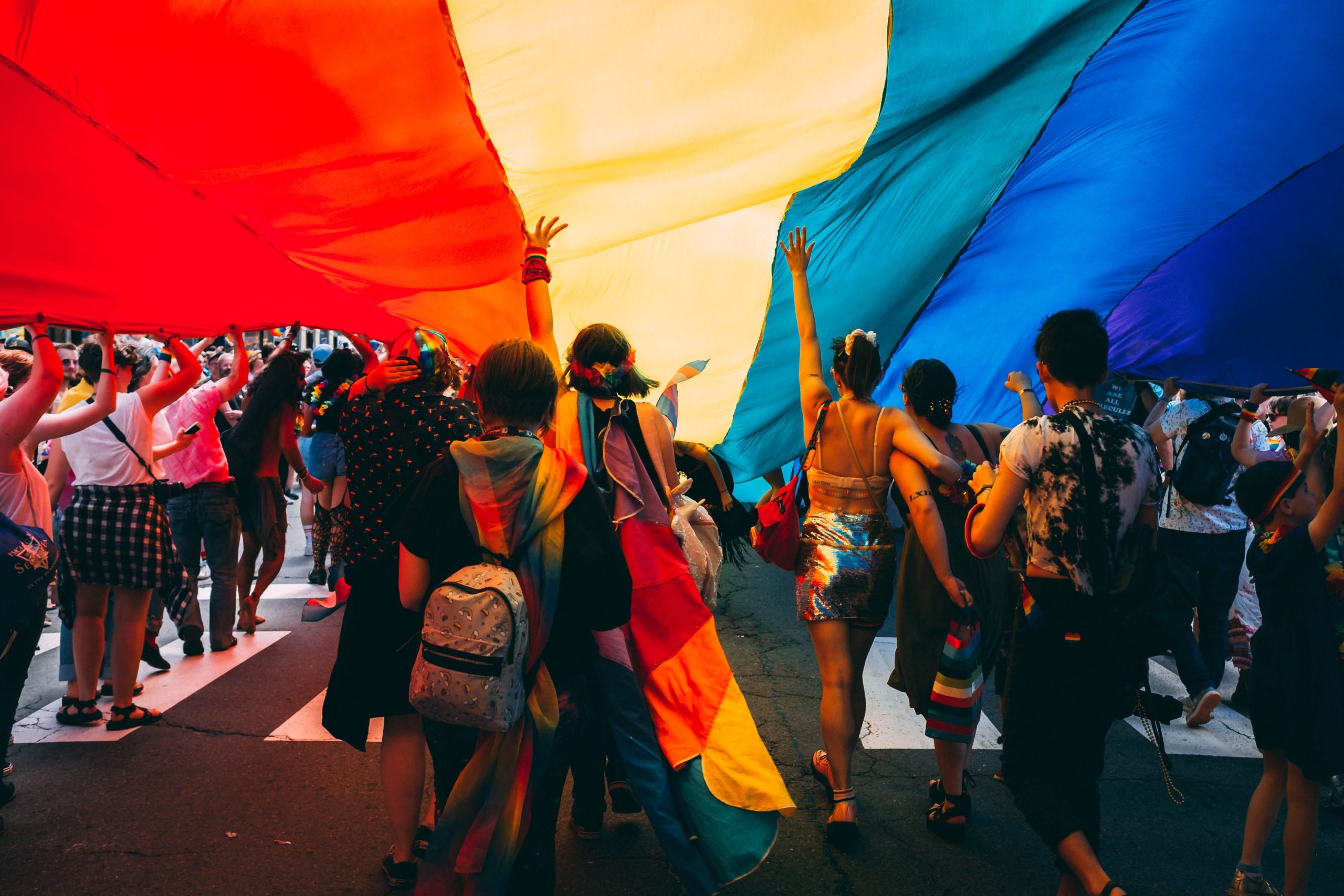 A group of people walk beneath a giant rainbow flag.